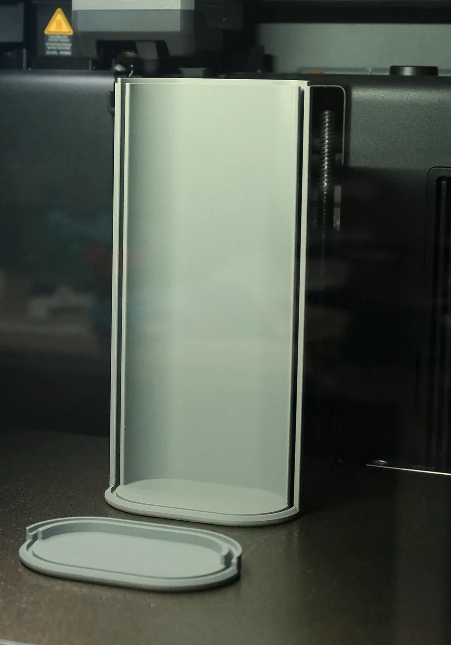 A rolling lid stationery box on a printer bed: the tall body standing upright and its oval base lying loose beside it, one file that contains two separate parts and was always meant to
